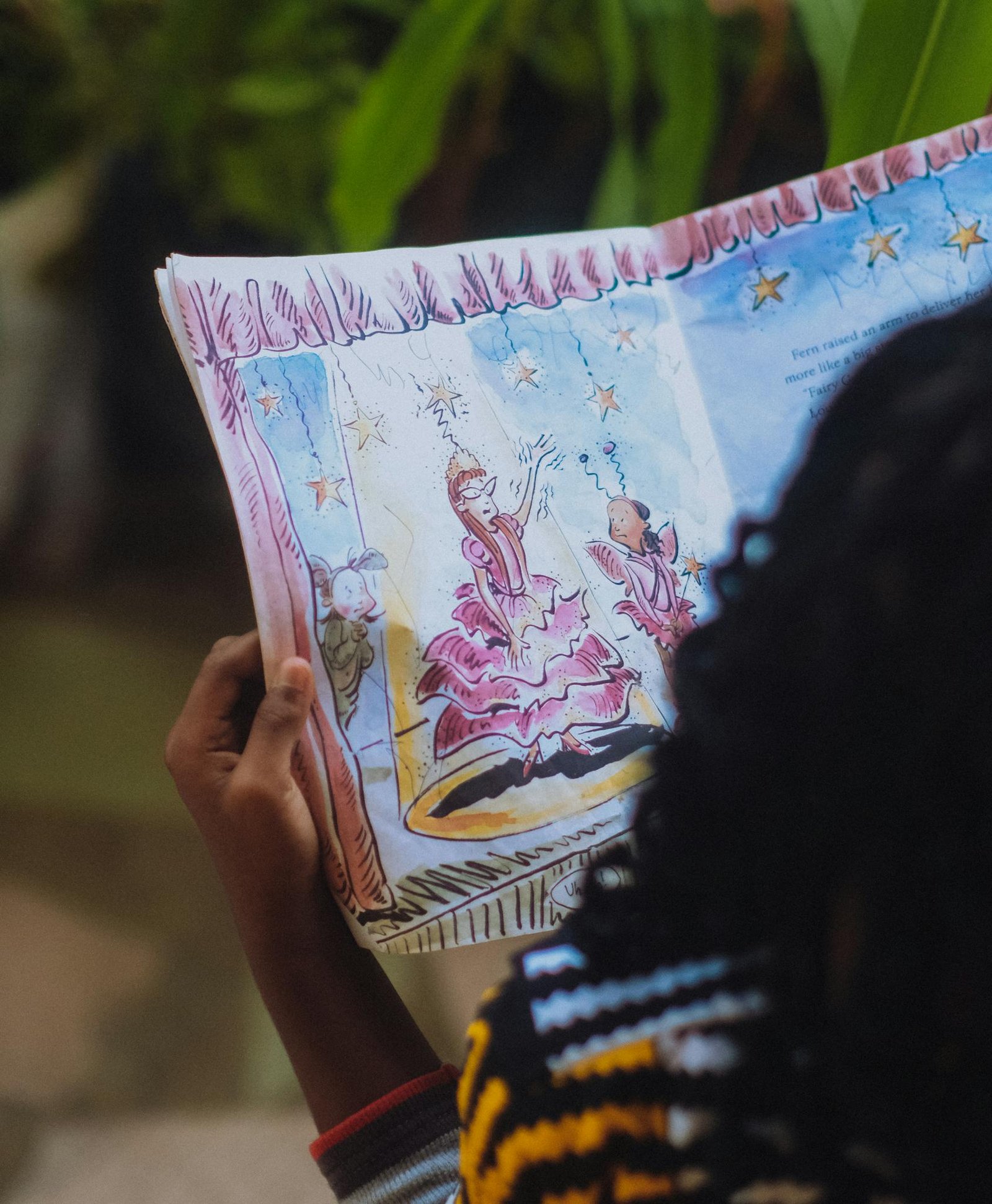 A child reads an illustrated storybook outdoors, captivated by colorful fairy-tale images.